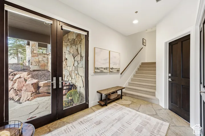 Stone tile flooring, dark wood-finish paneled doors, carpeted staircase, wood-finish handrail, recessed lighting