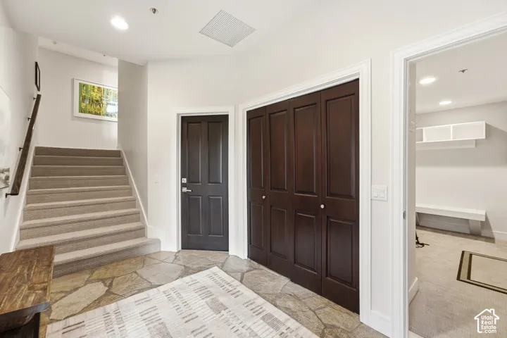 Flagstone flooring with carpeted stairs, dark panel doors, bi-fold closet doors, and recessed lighting