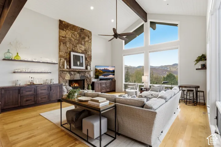 Vaulted ceiling with exposed beams, stone fireplace, expansive windows, wood-finish flooring, and built-in cabinetry