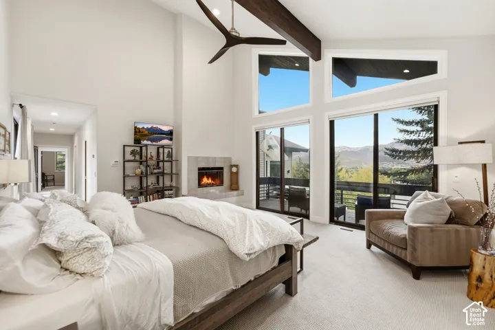 Vaulted ceiling with exposed wood beams, fireplace with stone surround, large format windows, glass sliding doors, and light-tone carpeting