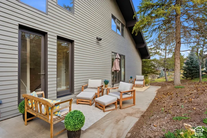 Exterior featuring horizontal siding, multiple glass panel doors, a concrete patio, and a sloped, natural landscaping area