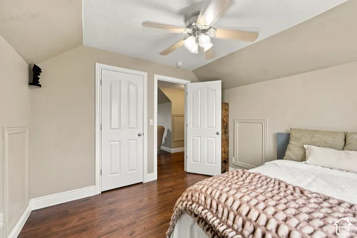 Room featuring wood-finish flooring, vaulted ceilings, a ceiling fan with integrated lighting, and white six-panel doors