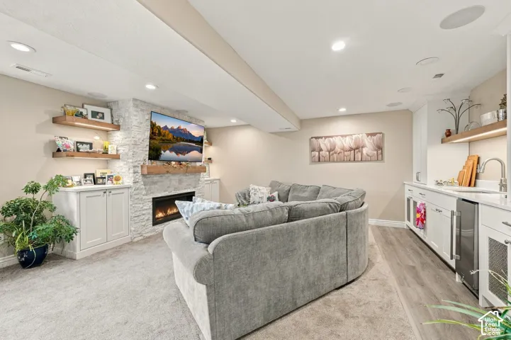 Fireplace featuring a stacked stone surround and wood mantel, integrated cabinetry, recessed lighting, and a built-in wet bar with wood-finish flooring