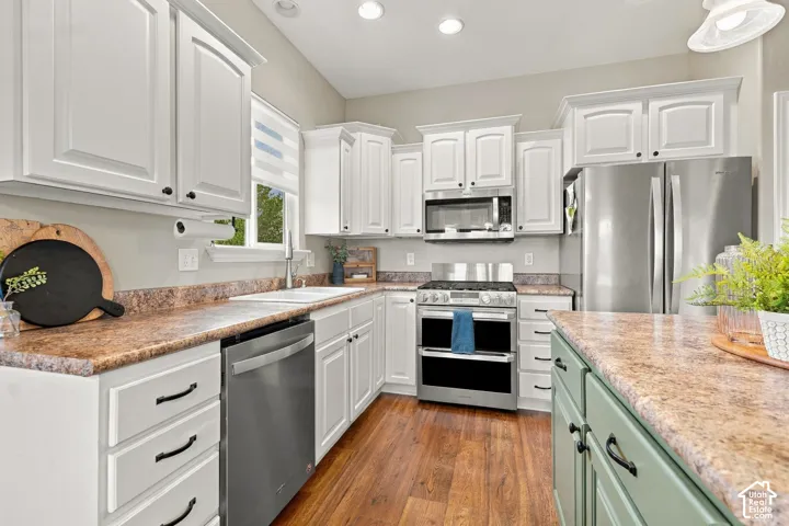 Kitchen featuring white shaker-style cabinetry, wood-finish flooring, stone-patterned countertops, stainless steel appliances, and a central island with sage-toned lower cabinetry