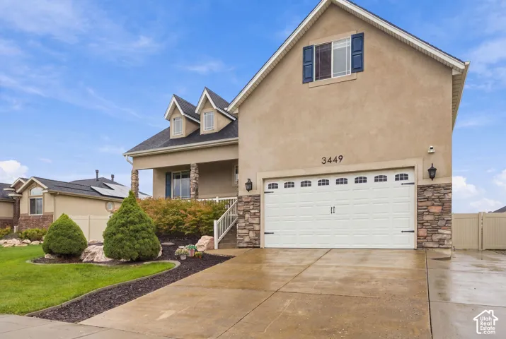 Stucco exterior featuring dual gabled dormers, decorative stone masonry accents, a two-car garage, and manicured landscaping