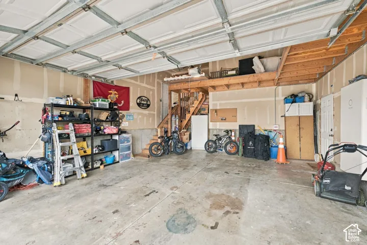 Multi-car garage featuring a concrete floor, overhead sectional door, and an integrated wooden loft storage area with staircase access