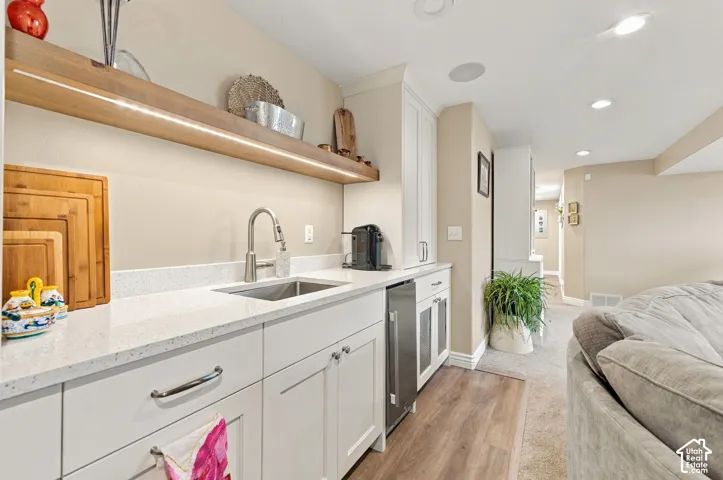 Wet bar featuring white cabinetry, quartz countertop, stainless steel under mount sink, under-cabinet lighting, and built-in under-counter refrigerator