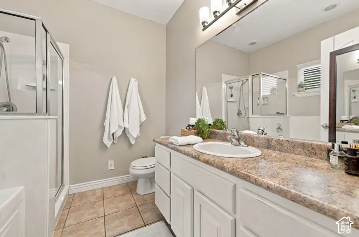 Bathroom featuring a white vanity with a composite countertop, an integrated sink, a glass-enclosed shower, tile flooring, and a full-width vanity mirror