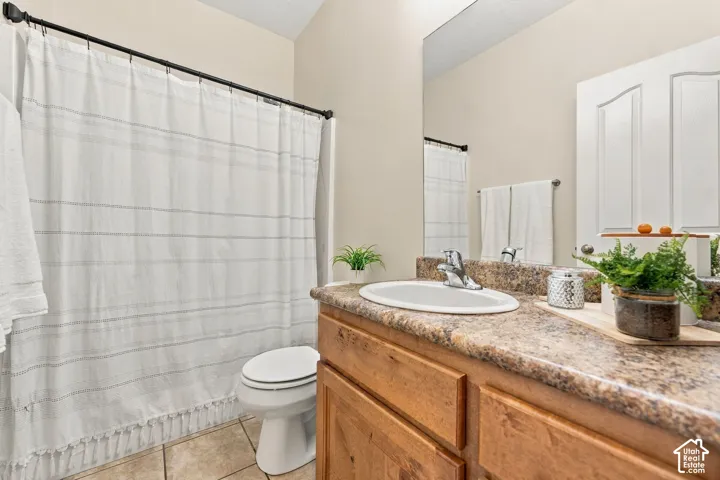 Main floor bathroom featuring a wood-finish vanity with a stone-composite countertop, oval drop-in sink, polished chrome faucet, and tile flooring