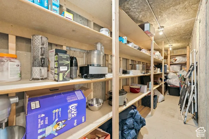 Storage area featuring concrete walls, exposed ceiling, and multiple levels of built-in wooden shelving
