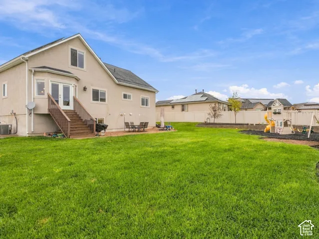 Expansive backyard featuring a manicured lawn, stone-paved patio, wooden staircase with railing, and a fenced perimeter