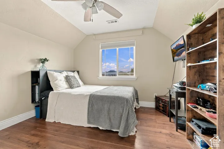 Sloped ceiling with wood-finish flooring, ceiling fan, and sliding window