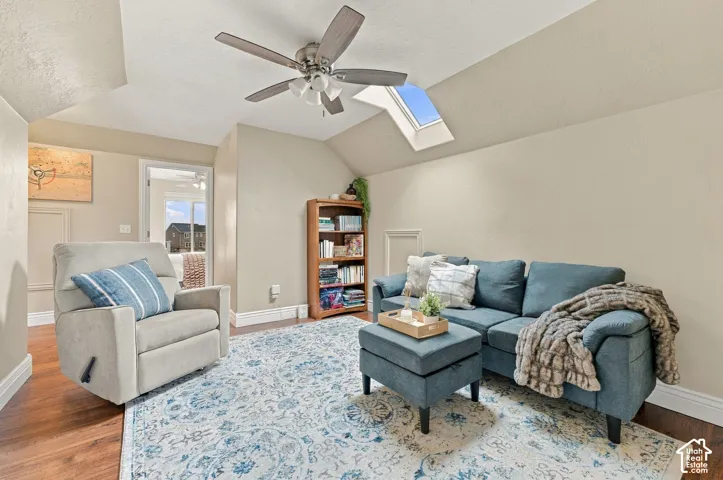 Vaulted ceiling room featuring a skylight, wood-finish flooring, and a ceiling fan with integrated lighting
