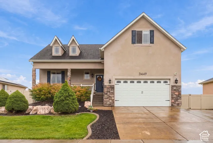 Stucco exterior featuring dual gables, stone veneer accents, a covered front porch, and a two-car garage