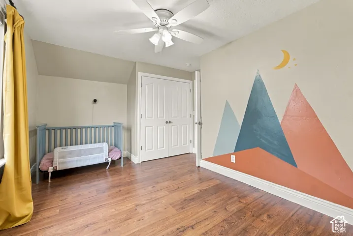 Room featuring wood-finish flooring, a ceiling fan with integrated lighting, and dual-panel closet doors