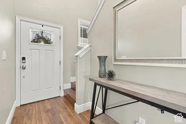 Entryway featuring wood-finish flooring, a white paneled front door with a glass insert, and a staircase with a wooden handrail and trim