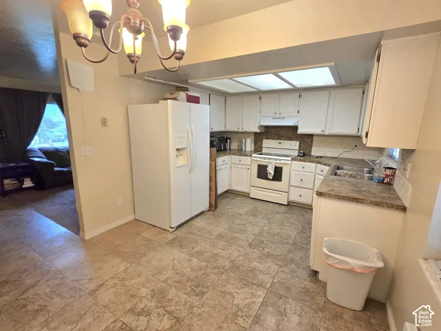 Kitchen featuring white cabinetry, stone-finish countertops, tile flooring, a multi-bulb chandelier, and integrated recessed lighting
