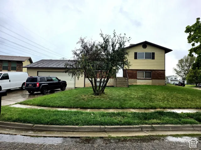 Split-level exterior featuring a brick and horizontal siding facade, metal roofing, an attached garage, and a concrete driveway
