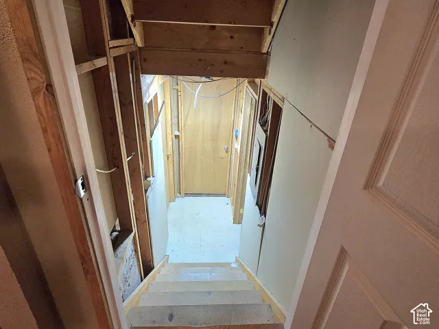 Staircase featuring exposed wood framing, unfinished walls, a solid wood door, and an electrical service panel