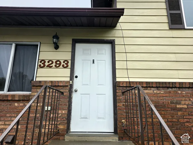 Exterior entrance featuring horizontal lap siding, a brick masonry facade, metal handrails, and an exterior wall-mounted light fixture