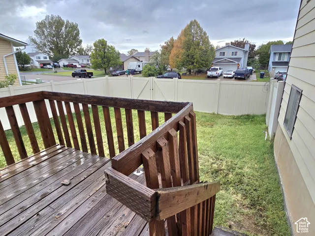 Raised wood deck with integrated stairs and vertical balusters, enclosed by perimeter vinyl fencing surrounding a grass yard