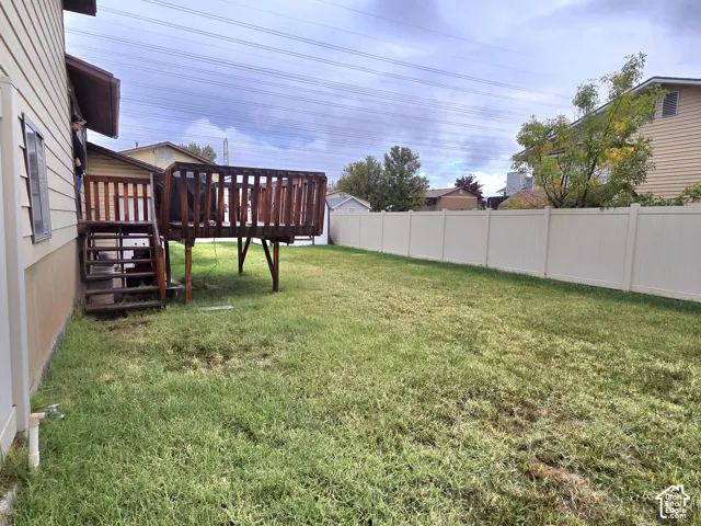 Private backyard featuring a wood deck with stairs, a lawn, and surrounding vinyl fencing