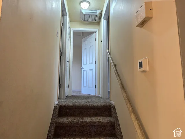 Staircase with wall-mounted handrail, featuring carpeted steps and multiple paneled interior doors