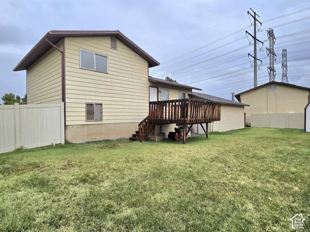 Two-story structure featuring horizontal siding, a raised wood deck, and a vinyl perimeter fence
