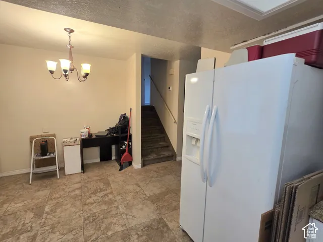 Interior space featuring neutral-toned tile flooring, a multi-arm chandelier with glass shades, and a side-by-side refrigerator