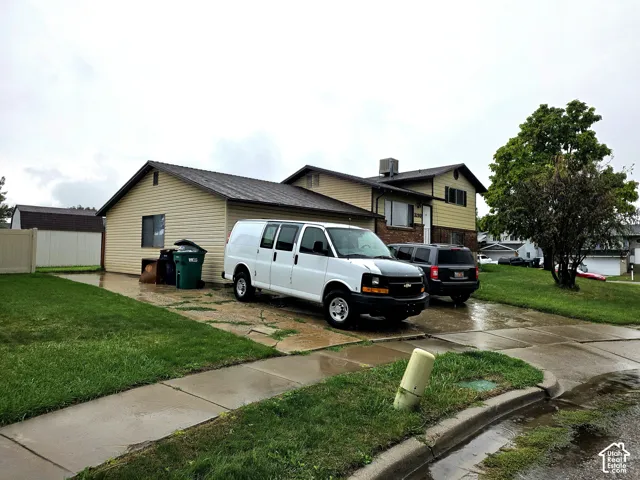 Split-level exterior featuring light-toned horizontal siding, a multi-gabled roofline, concrete driveway, and a detached storage structure