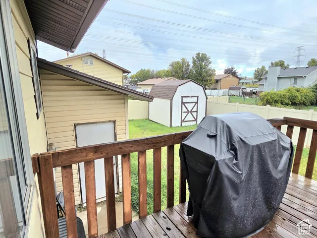Elevated wood deck with horizontal railing, vinyl siding exterior, and detached storage structure situated in a fenced yard