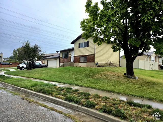 Split-level exterior featuring horizontal siding, brick veneer foundation, attached garage, and mature trees on a corner lot