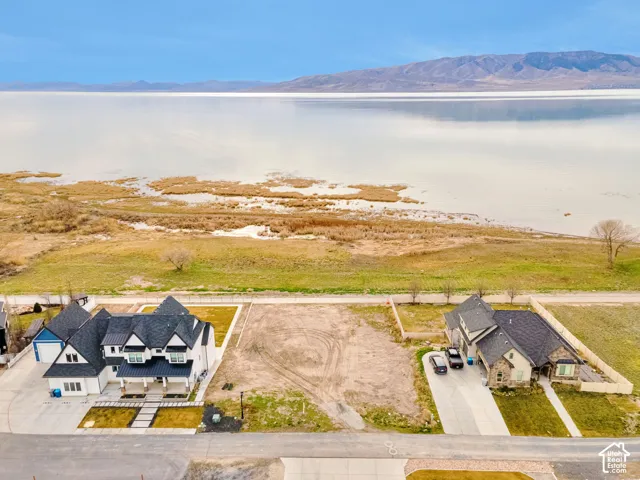 Aerial perspective of lakefront property featuring expansive water frontage, mountain backdrop, and direct paved road access
