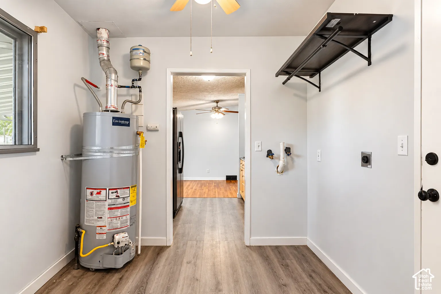 Utility room featuring wood-finish flooring, a wall-mounted shelving unit, an electric water heater, and washer and dryer utility hookups