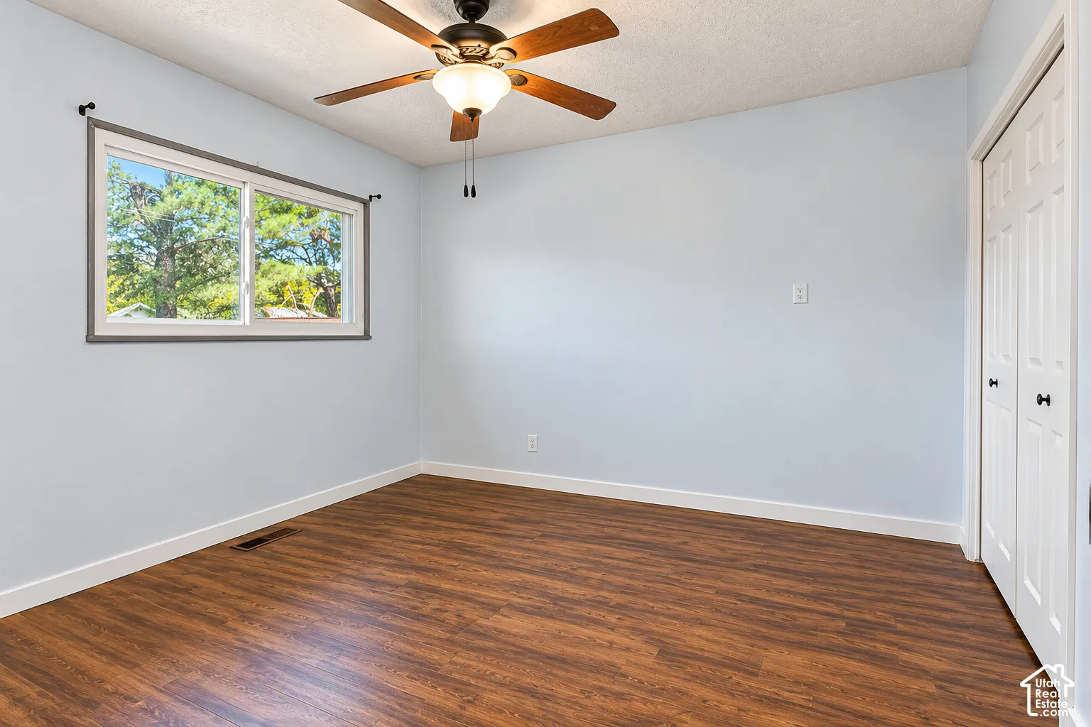 Room featuring wood-finish flooring, a horizontal sliding window, a ceiling fan with integrated lighting, and dual-panel closet doors