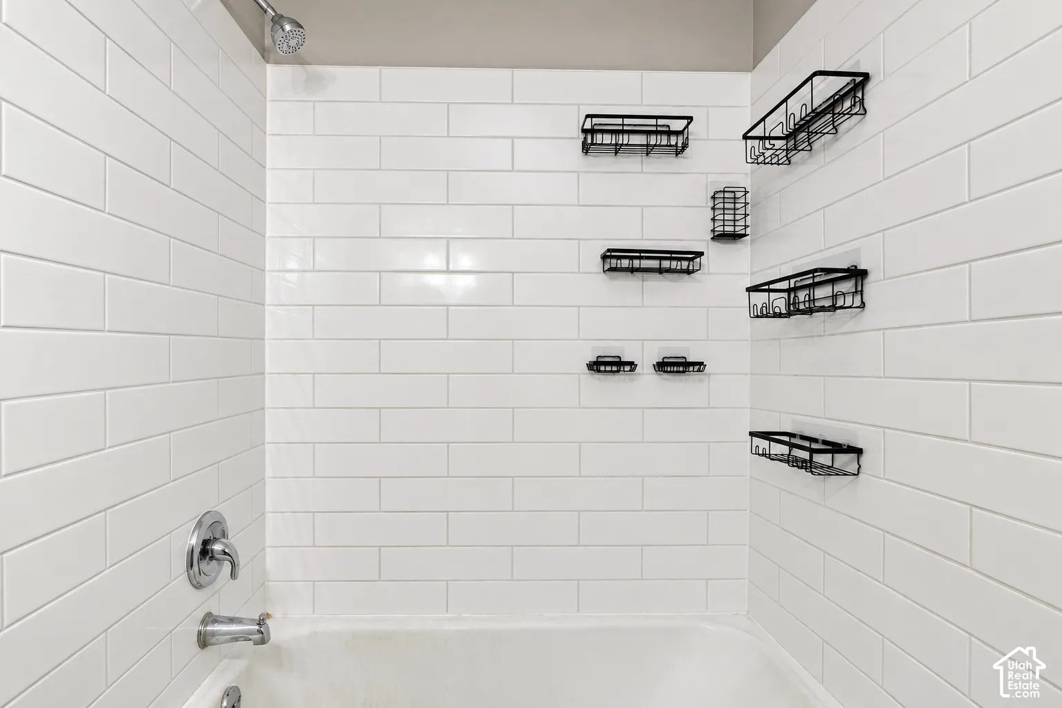 Shower area featuring white subway tile wall surround, chrome fixtures, and mounted metal storage racks