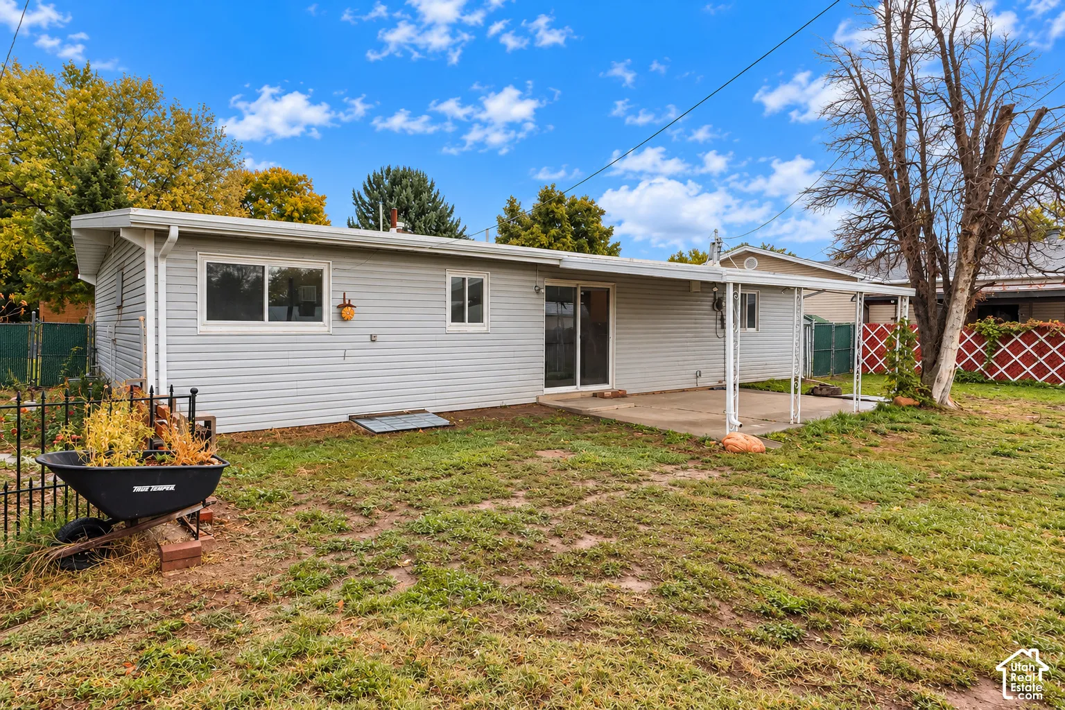 Exterior rear elevation featuring light-toned horizontal siding, a covered concrete patio, and fenced yard space