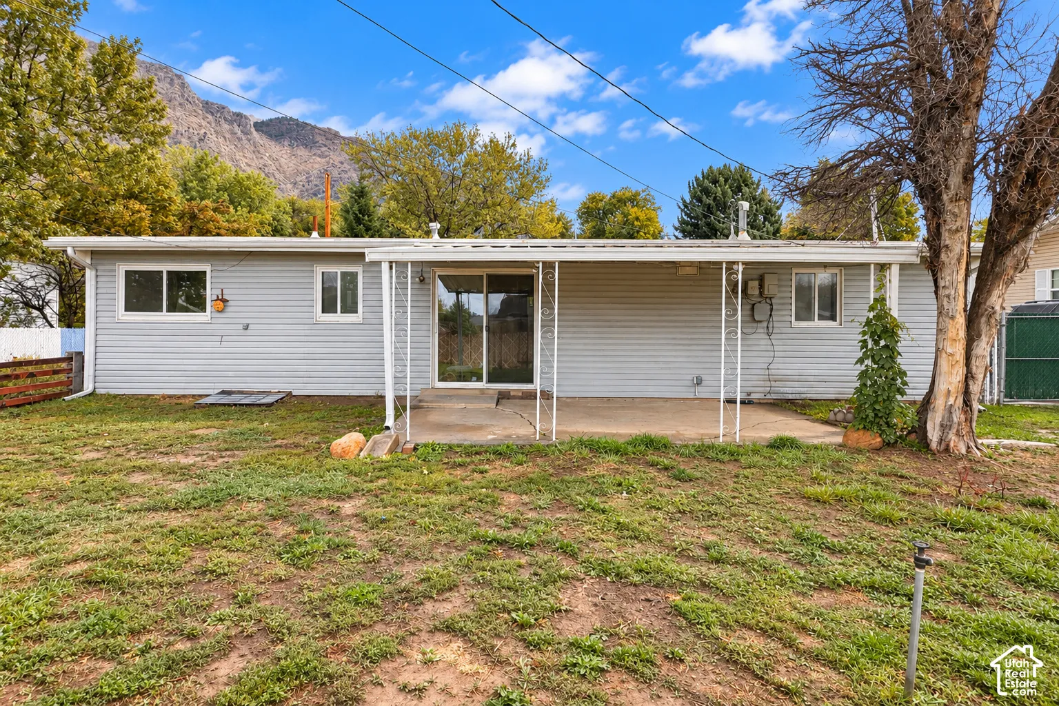 Single-story exterior with light-colored horizontal siding, covered concrete patio, sliding glass door, and mountain backdrop