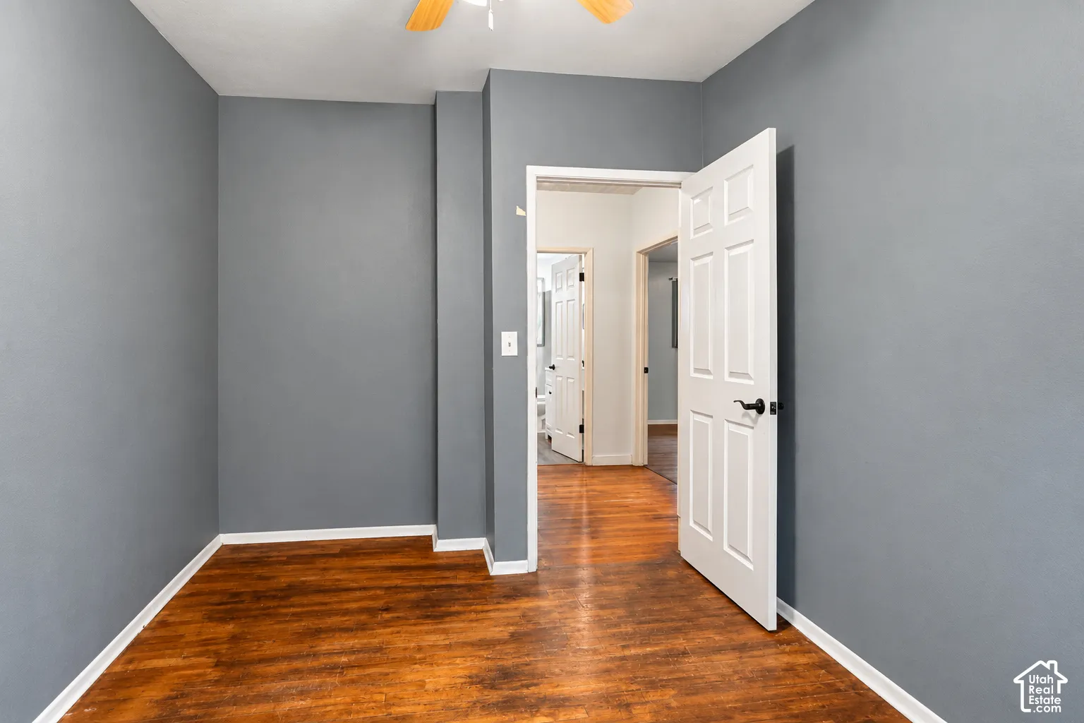 Room featuring wood-finish flooring, six-panel door with matte black hardware, and ceiling fan