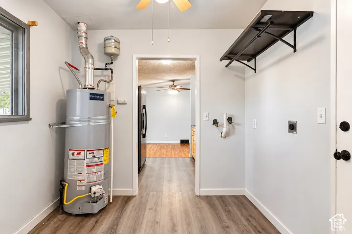 Utility room featuring wood-finish flooring, a wall-mounted shelving unit, an electric water heater, and washer and dryer utility hookups