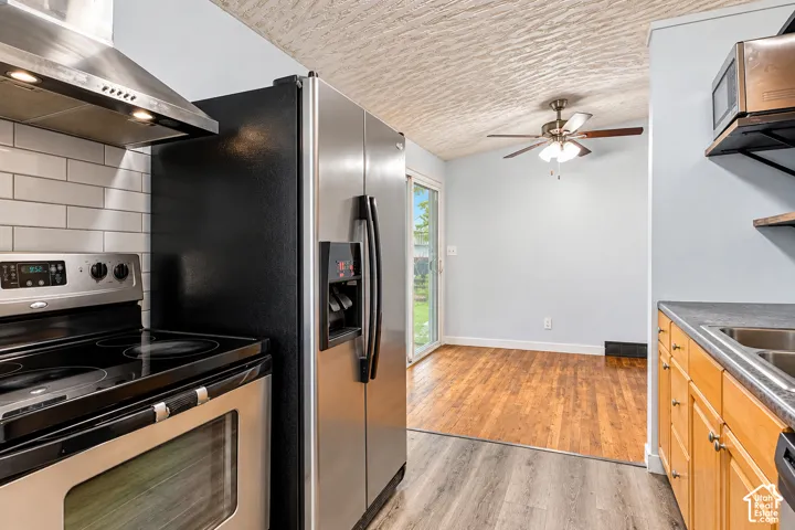 Kitchen featuring stainless steel appliances, white subway tile backsplash, wood-finish flooring, ceiling fan, and sliding glass door