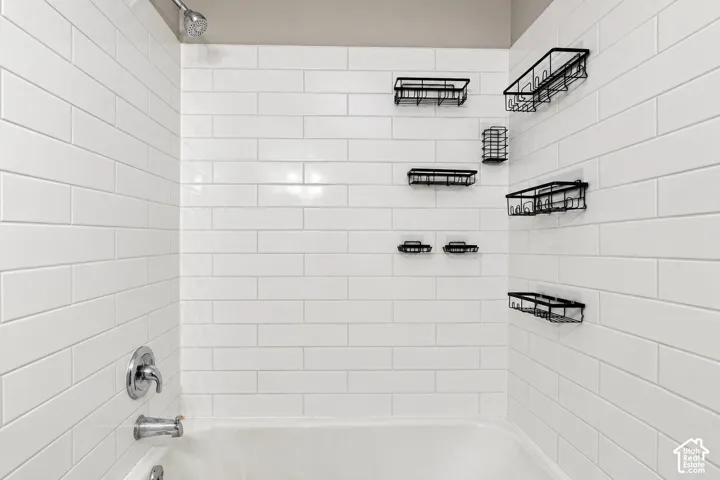 Shower area featuring white subway tile wall surround, chrome fixtures, and mounted metal storage racks