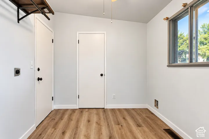 Interior space featuring wood-finish flooring, two white interior doors, a window with a neutral-toned frame, and a ceiling-mounted fan fixture