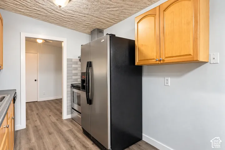 Kitchen featuring wood-finish flooring, wood cabinetry, stainless steel refrigerator, and grey tile backsplash