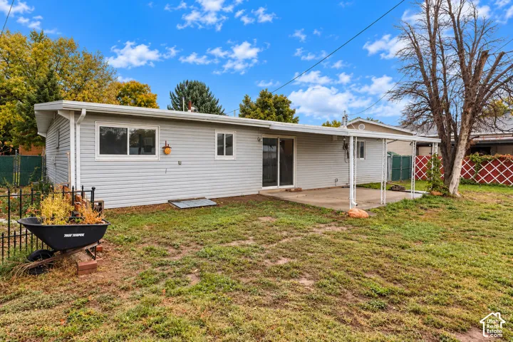 Exterior rear elevation featuring light-toned horizontal siding, a covered concrete patio, and fenced yard space