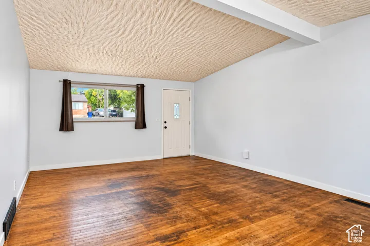 Interior room featuring wood-finish flooring, a vaulted ceiling with exposed structural beam, and a single-entry door with glass insert