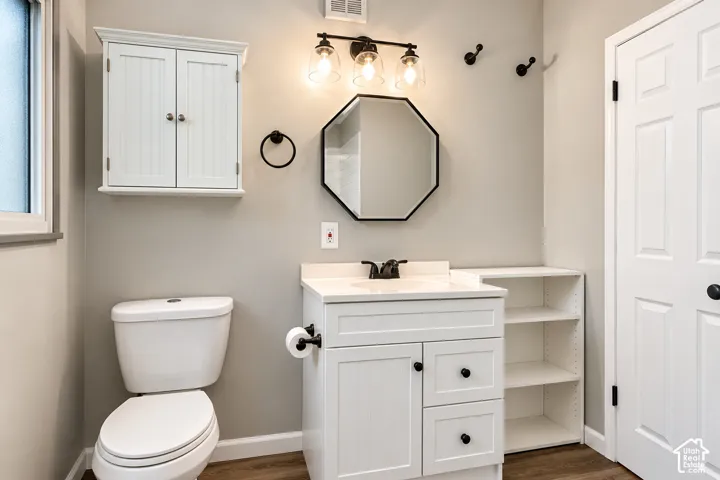 Vanity featuring a solid-surface countertop, white cabinetry with built-in open shelving, an octagonal mirror, wall-mounted three-light fixture, and matte black hardware