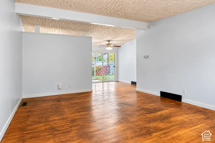 Interior space featuring wood-finish flooring, exposed structural ceiling beams, a textured ceiling finish, and a sliding glass door