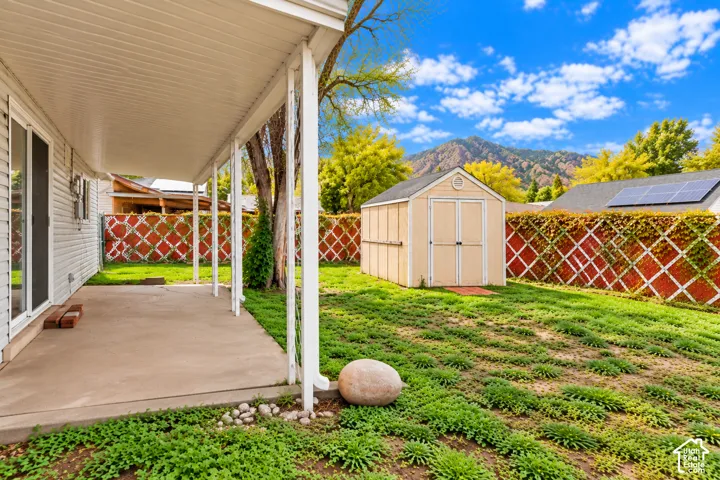 Covered concrete patio with a detached storage shed, privacy lattice fencing, and mountain backdrop