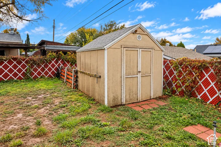 Backyard storage shed featuring a gabled roof, double doors, and red lattice fencing